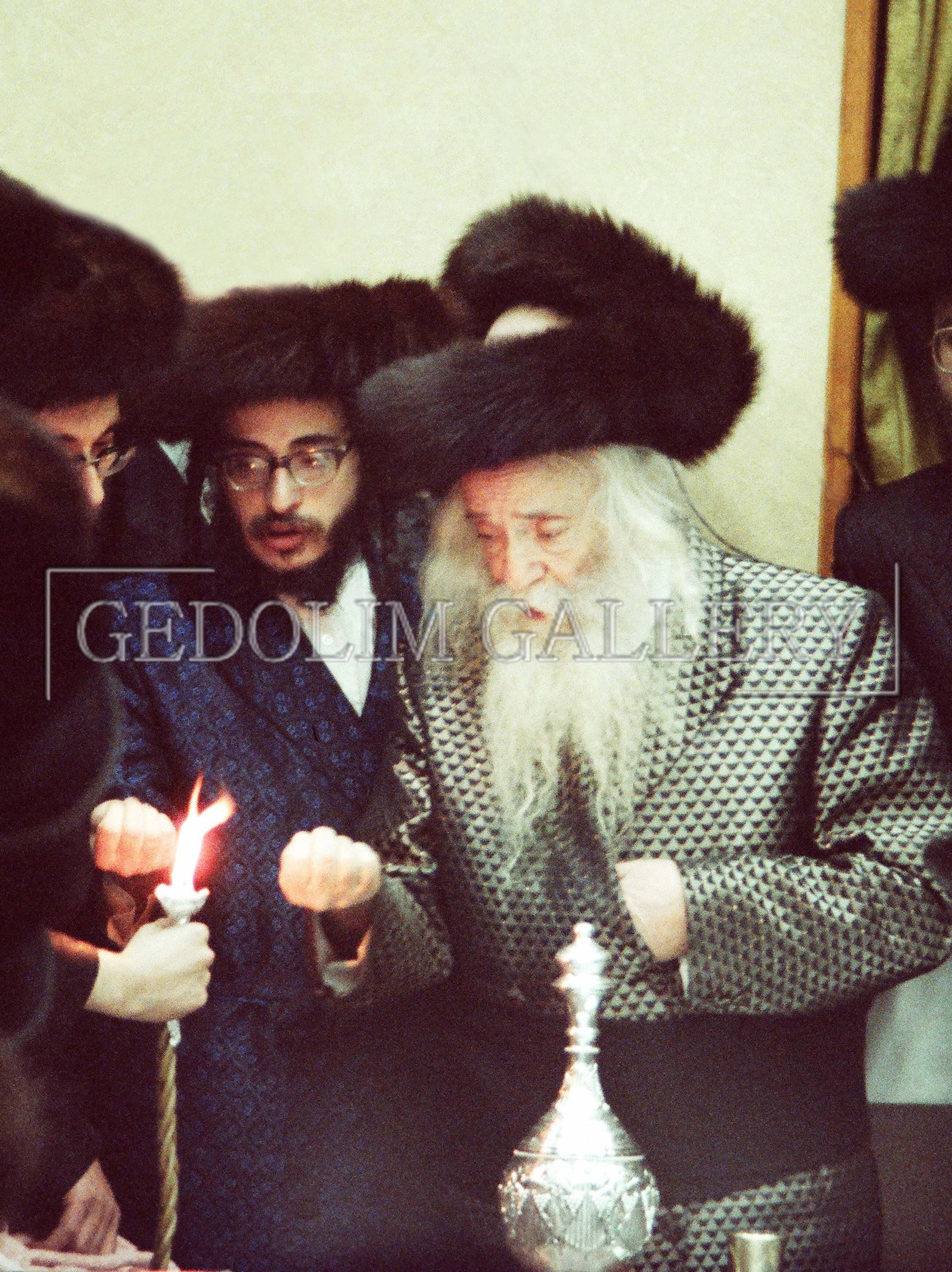 A man with a beard is holding a candle in front of a sign that says gedolin gallery