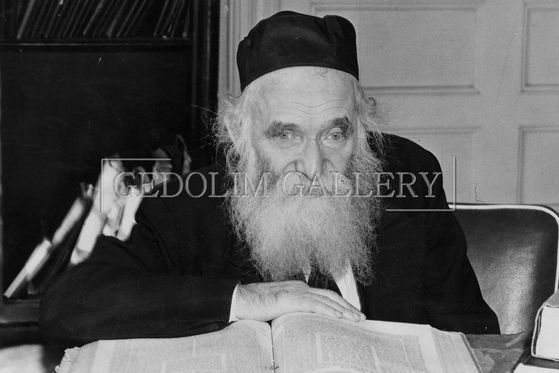 A man with a beard is sitting at a desk reading a book