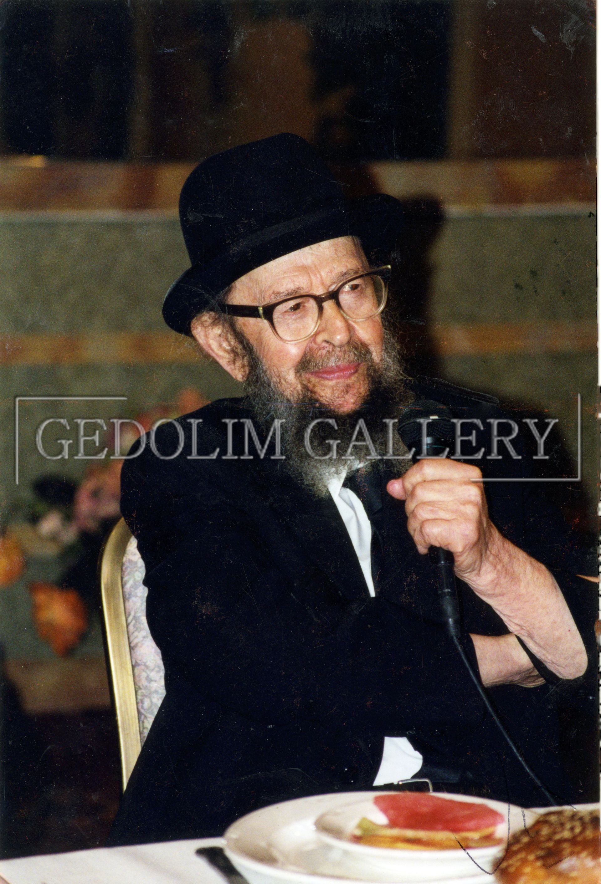 A man wearing a top hat and glasses is sitting at a table with a plate of food ..
