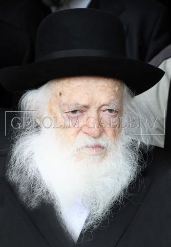 A man with a beard and a hat is wearing a black suit.