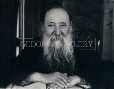 A man with a beard is sitting at a table with his hands folded.