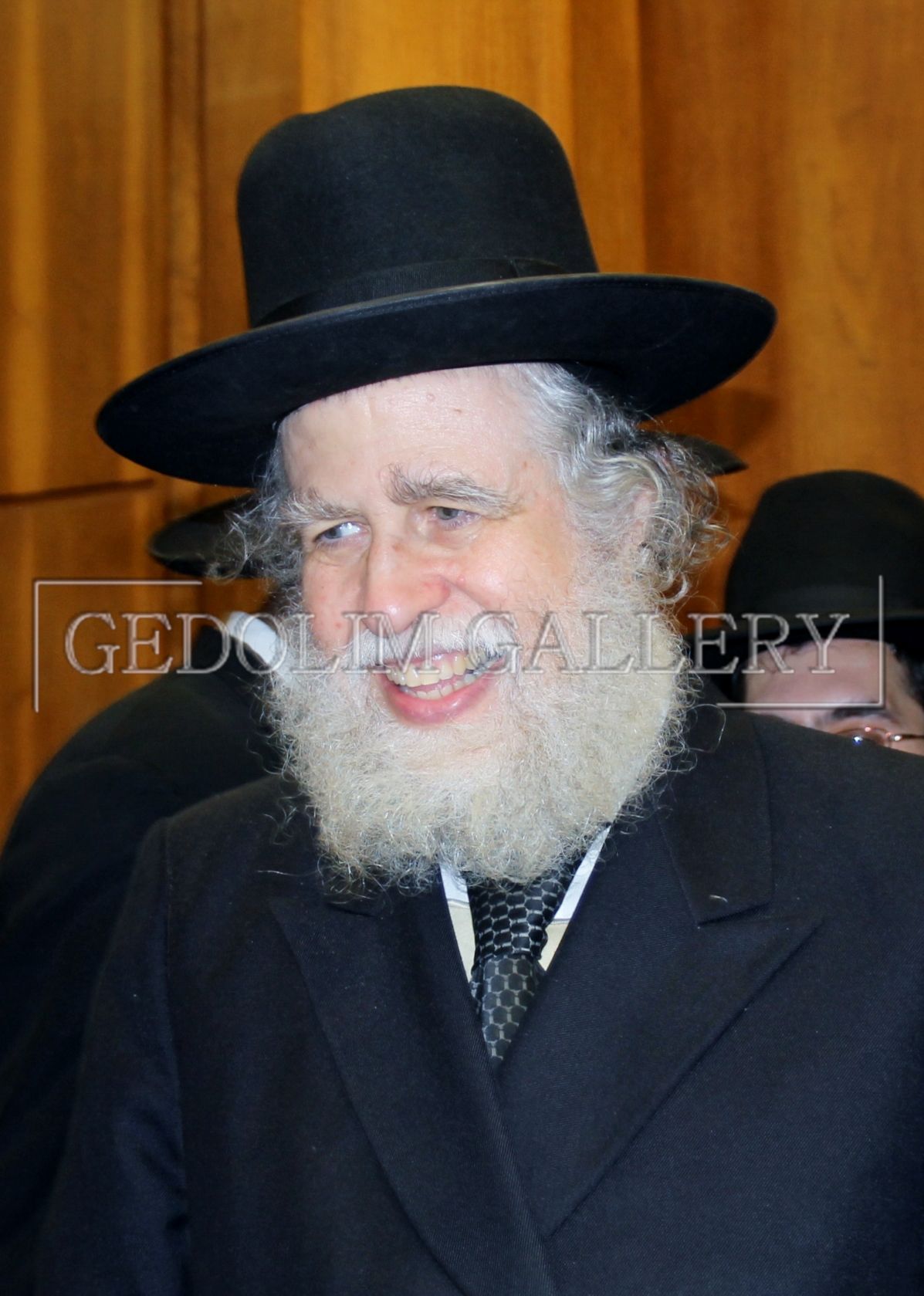A man with a beard wears a black hat and a black jacket