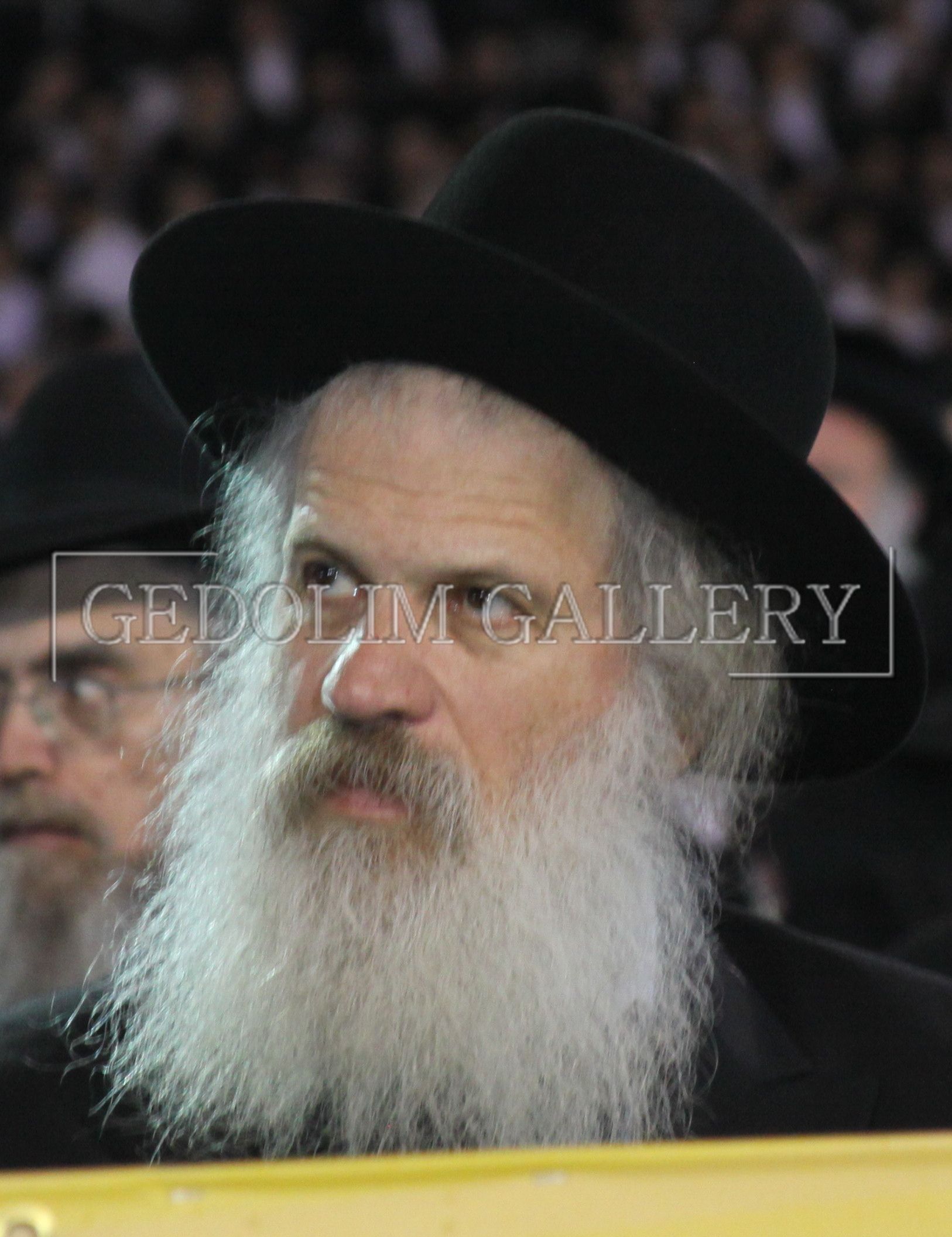 A man with a beard wearing a black hat is sitting in a crowd