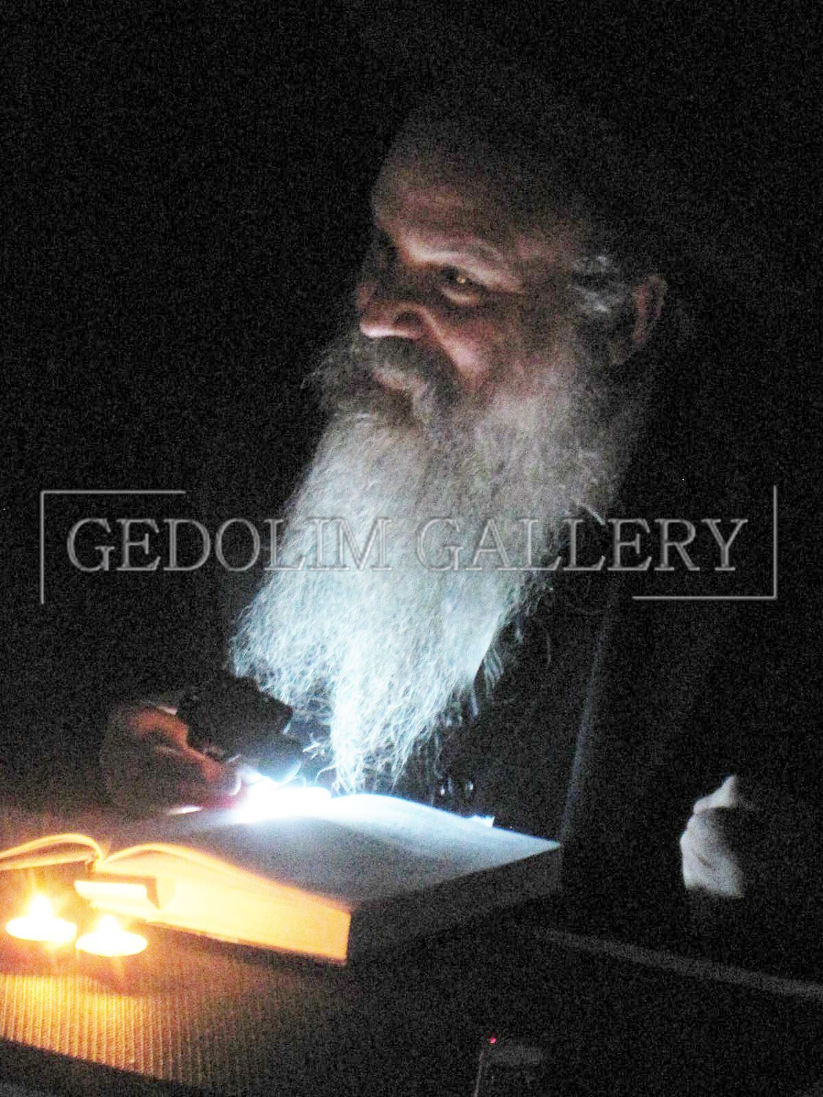 A man with a beard is reading a book with a flashlight in his hand ..