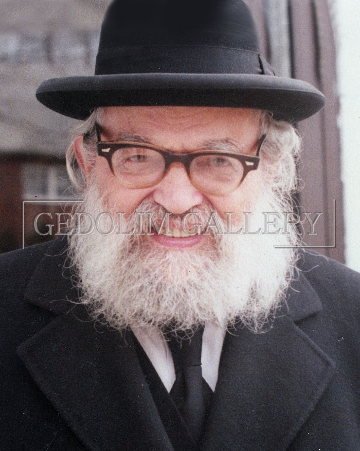 A man with a beard and glasses is wearing a black hat