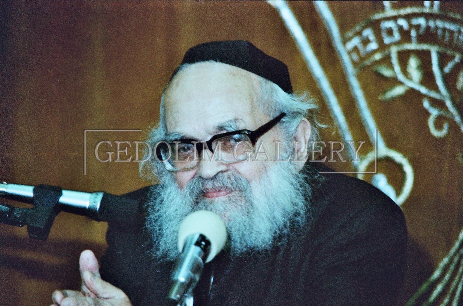 A man with glasses and a beard is speaking into a microphone