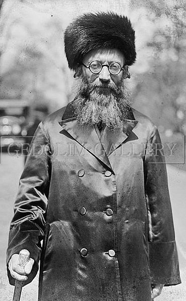 A black and white photo of a bearded man wearing a fur hat and holding a cane.