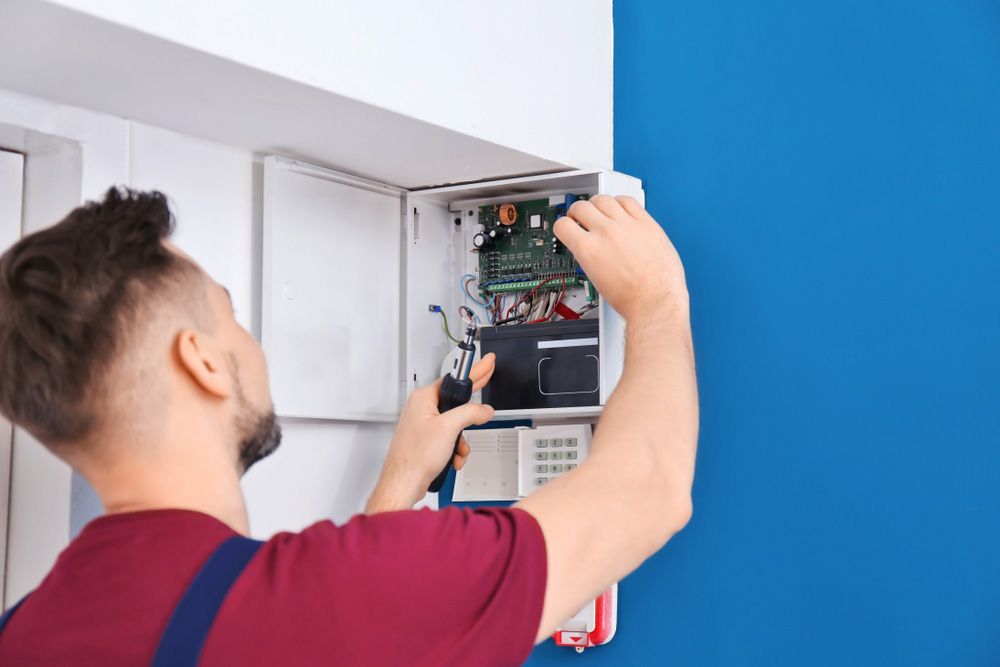 A Man Is Installing A Security System On A Blue Wall — Macleay Air In West Kempsey, NSW