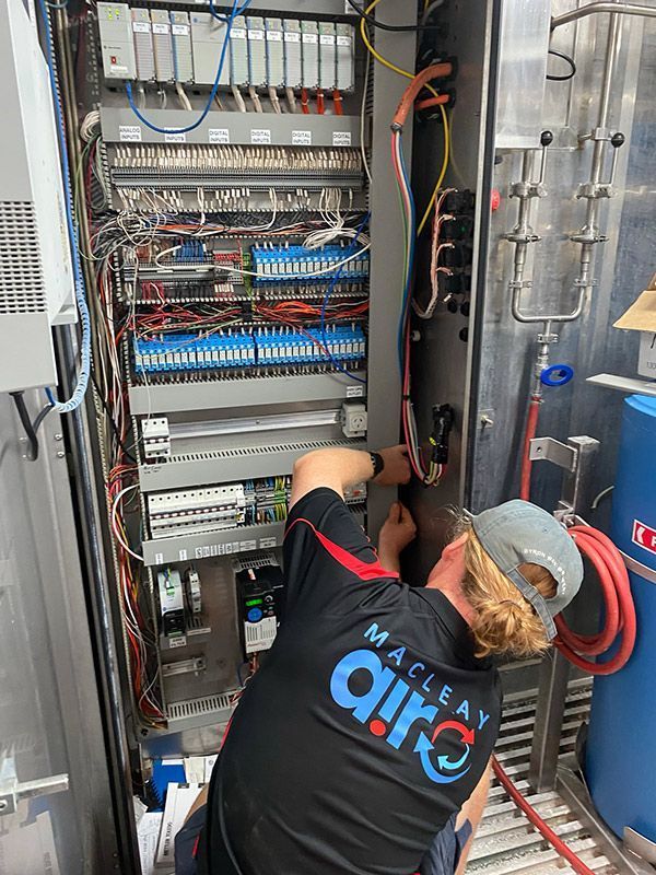 A Man Is Working On A Electrical Box In A Factory — Macleay Air In West Kempsey, NSW