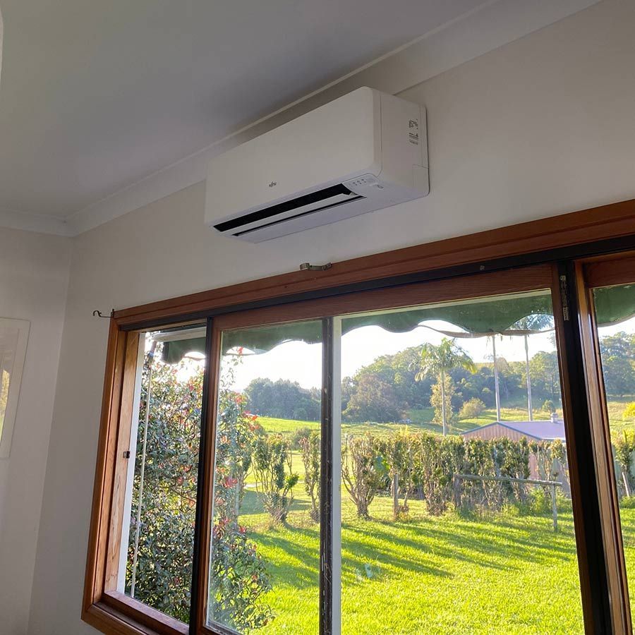 A Window With A View Of A Lush Green Field And Air Conditioner — Macleay Air In South West Rocks, NSW