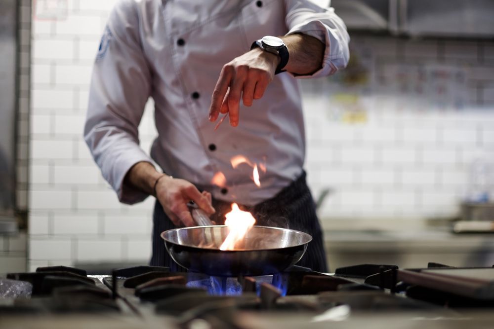 A Chef Is Cooking Food In A Wok On A Stove With Flames Coming Out Of It — Macleay Air In West Kempsey NSW