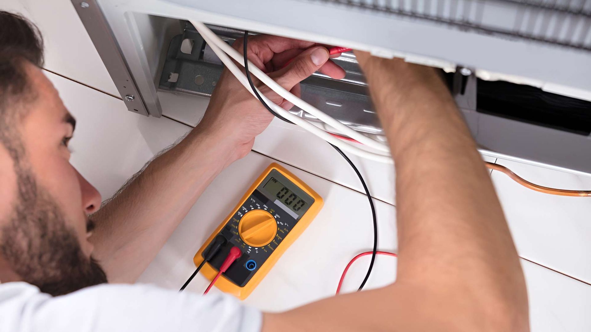 A Man Is Working On A Refrigerator With A Multimeter — Macleay Air In Macksville, NSW