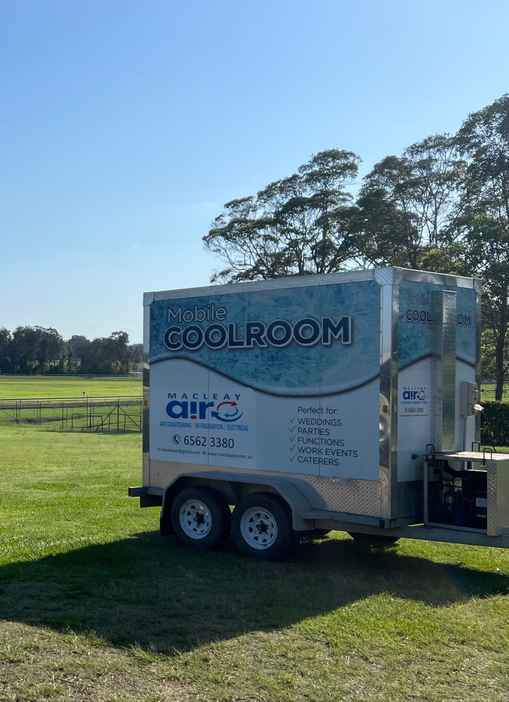 A cool room trailer is parked in a grassy field.