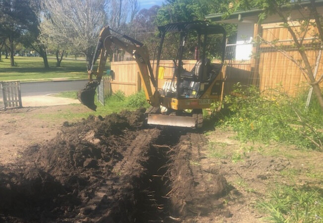 A small excavator is digging a hole in the dirt in front of a house.