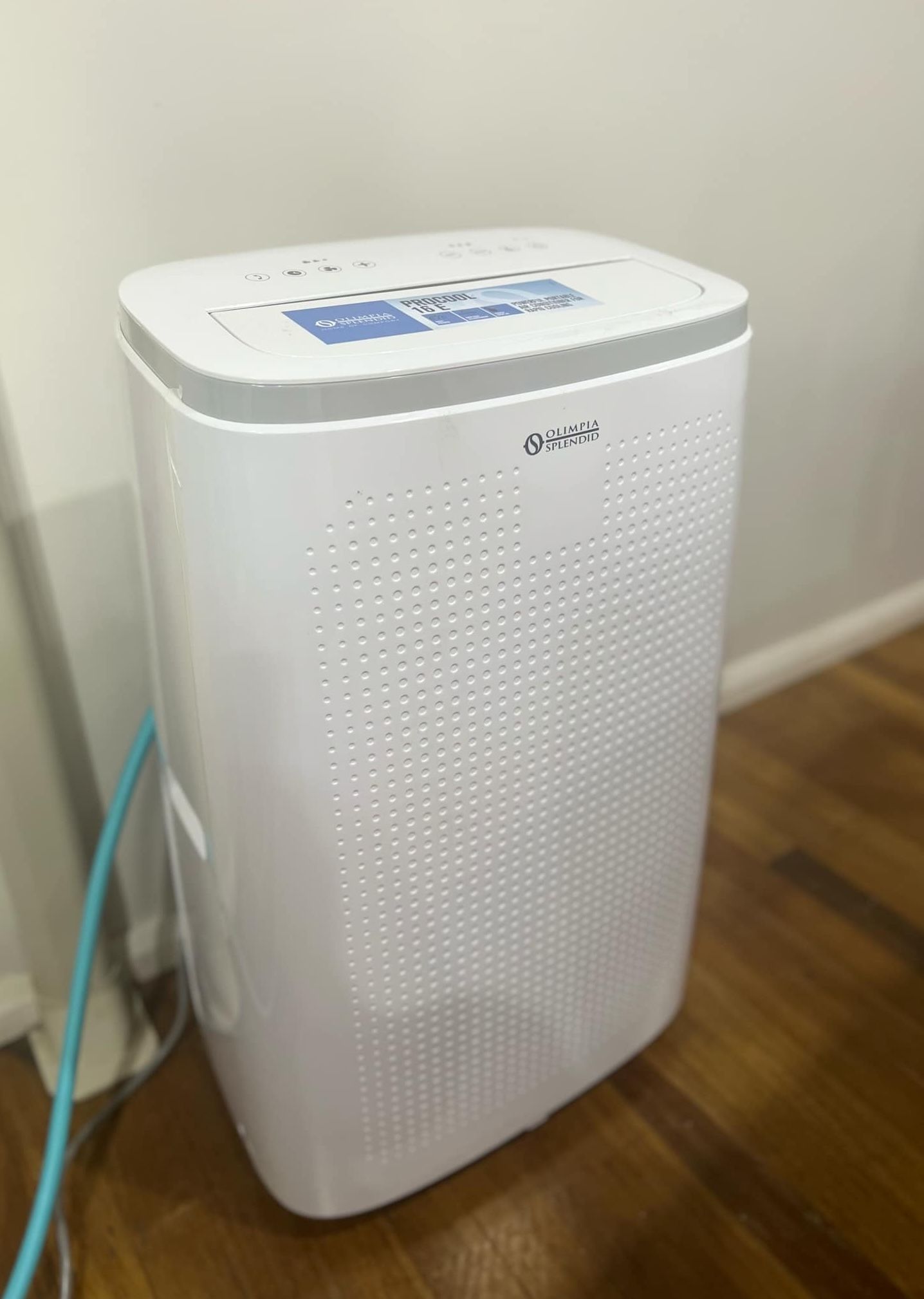 A white air purifier is sitting on a wooden floor next to a wall.