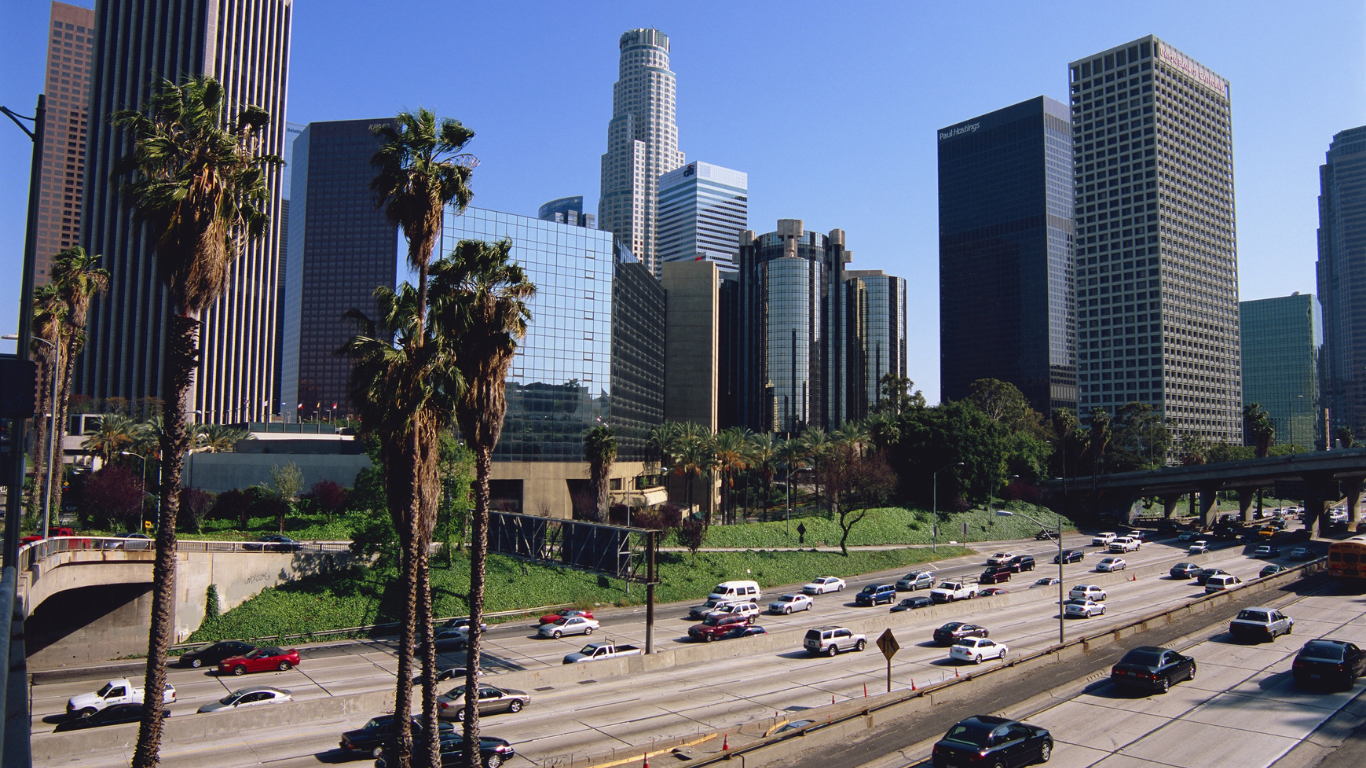 Los Angeles skyline with palm trees, freeway traffic, and blue sky.