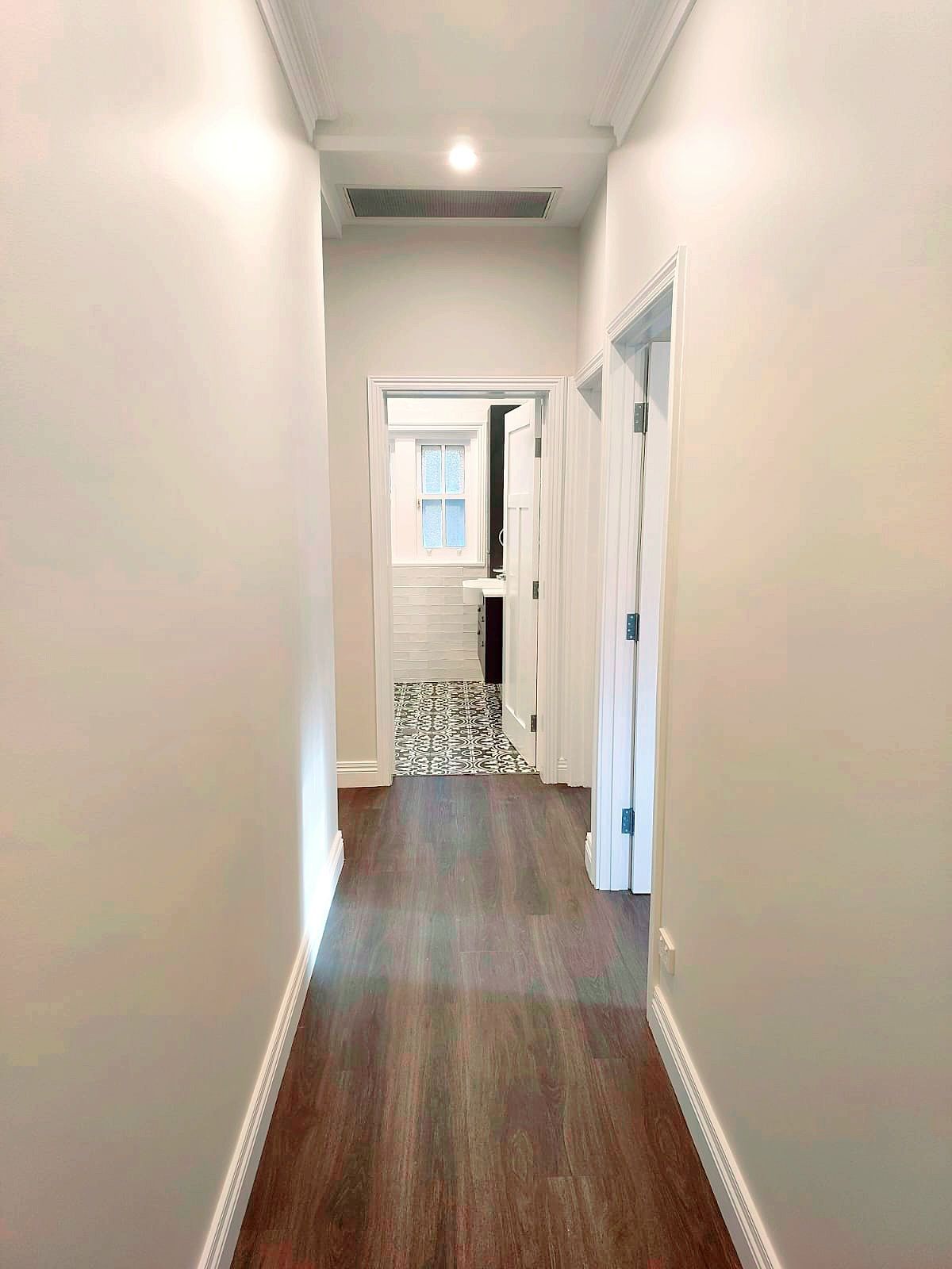 Narrow Hallway With Dark Wood-look Flooring and Doors Leading to Rooms, a Bathroom is Visible Ahead — Elimar Construction in Goulburn, NSW