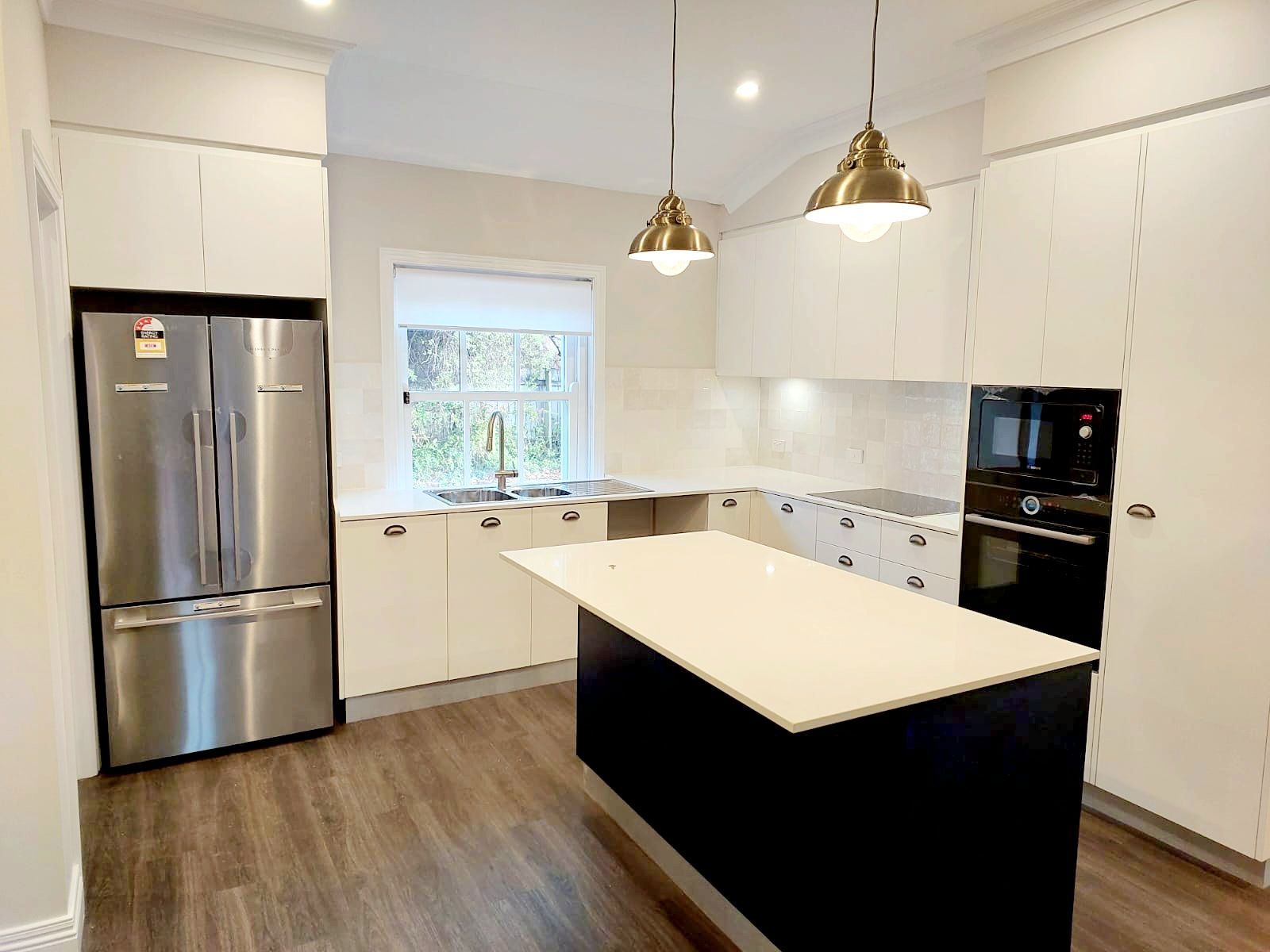 Modern White Kitchen With Stainless Steel Appliances, Dark Island, and Gold Pendant Lights — Elimar Construction in Goulburn, NSW