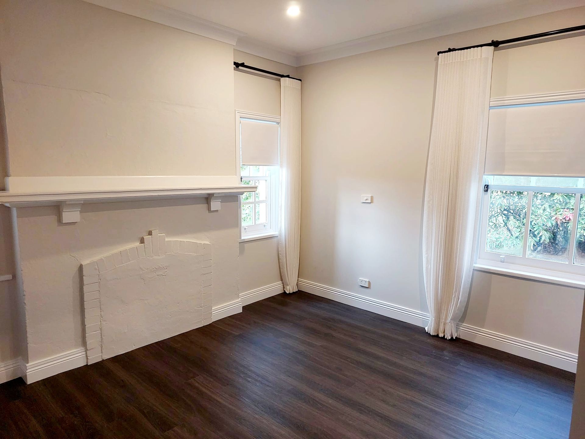 Empty Room With Fireplace, Dark Wood Floor, White Walls, and Two Windows With Sheer Curtains — Elimar Construction in Goulburn, NSW