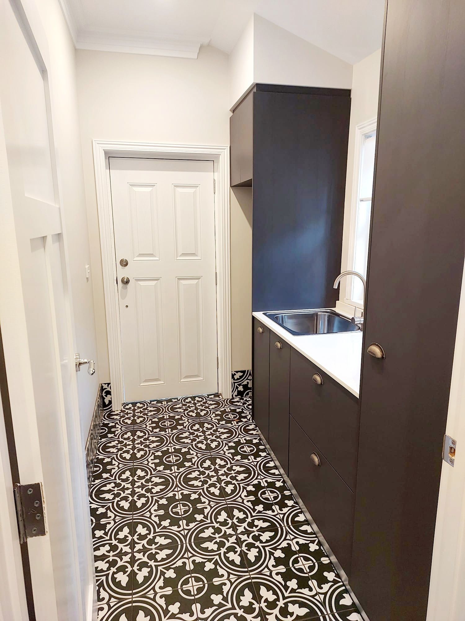 Narrow Laundry Room With Patterned Floor, Dark Cabinets, White Door — Elimar Construction in Goulburn, NSW