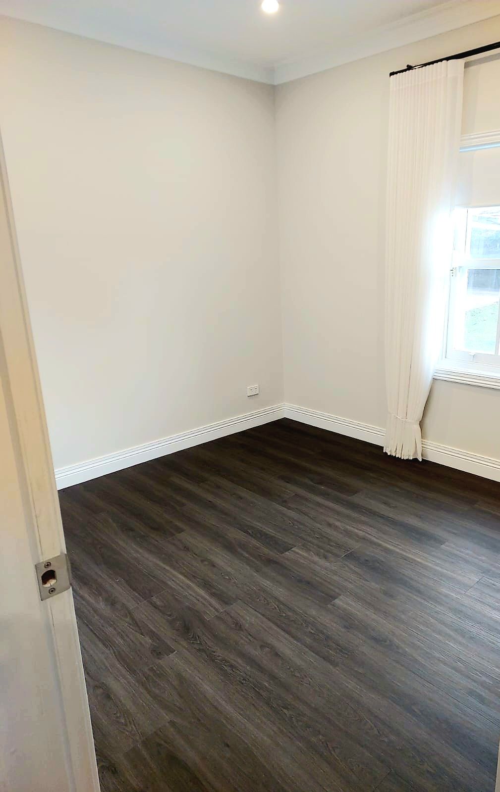 Empty Room With Dark Wood-look Flooring, White Walls, and a Window With Sheer Curtains — Elimar Construction in Goulburn, NSW