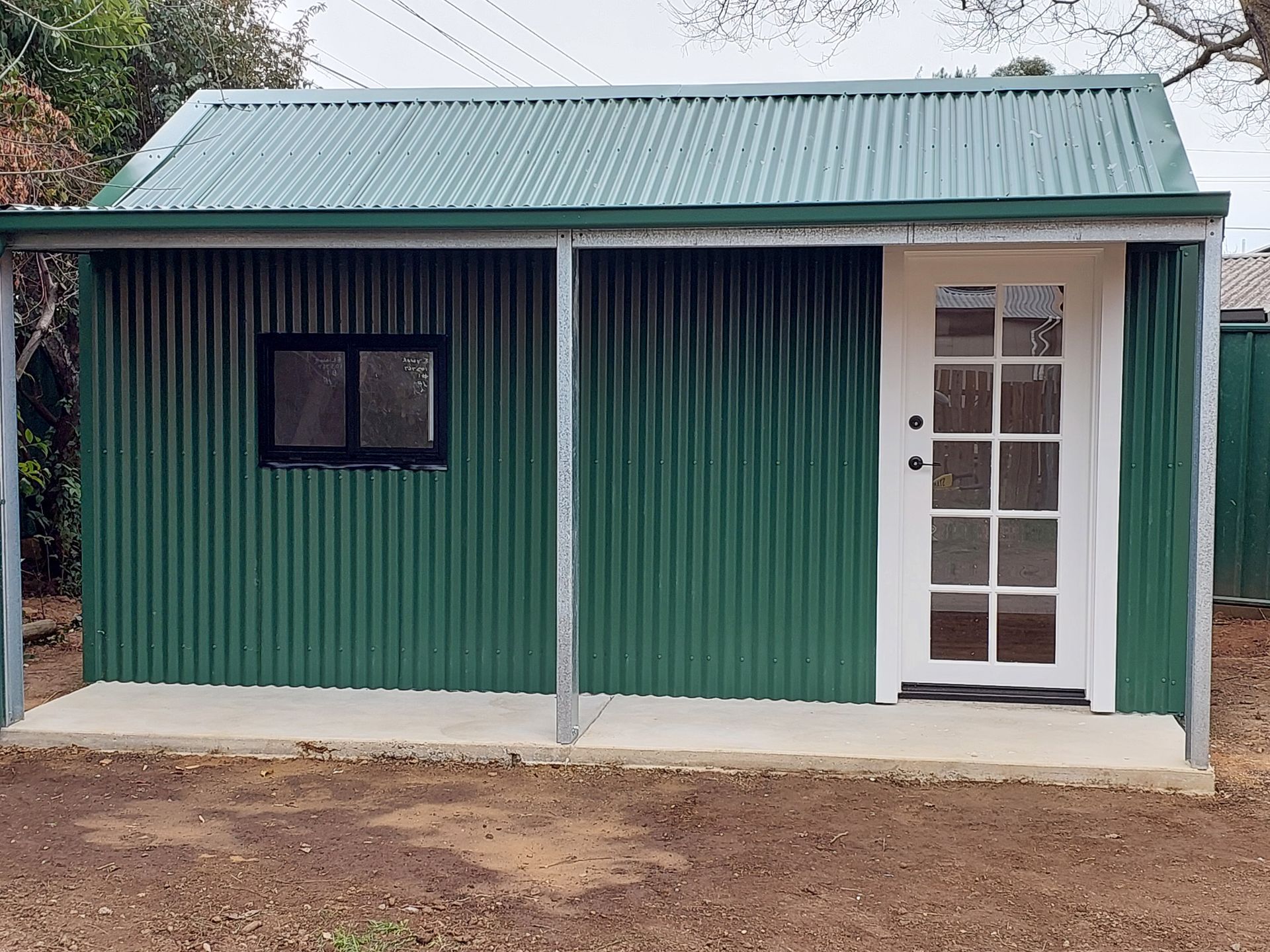 Green Corrugated Iron Shed With a White Door and Black Framed Window — Elimar Construction in Goulburn, NSW