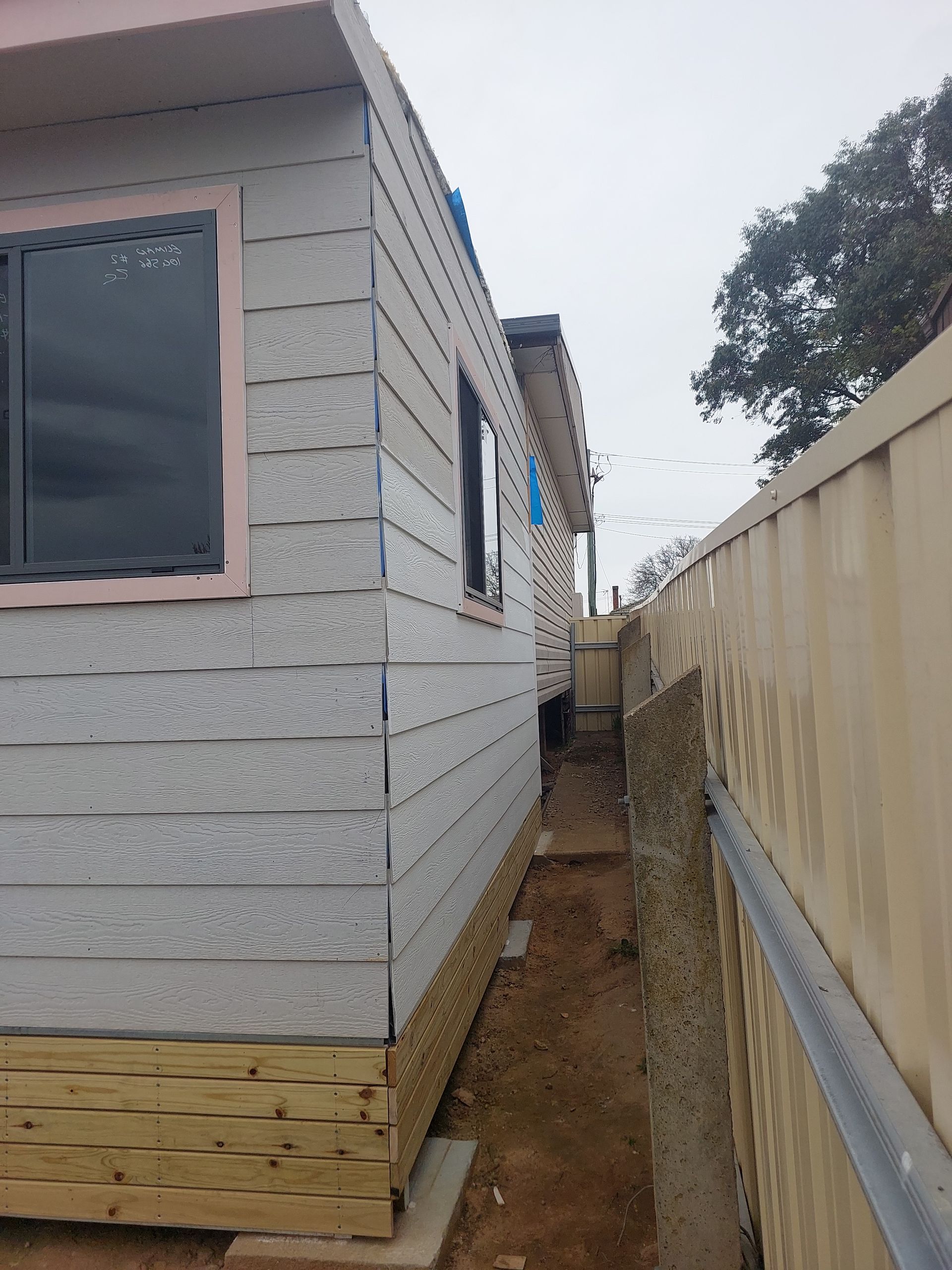 Side View of a Building With Light Gray Siding and a Dark Window Next to a Beige Fence, With a Narrow Walkway — Elimar Construction in Goulburn, NSW