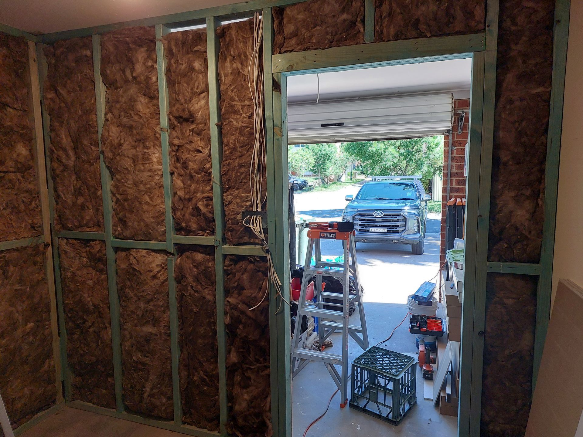 Interior Wall Under Construction With Insulation and Doorway, Leading to a Garage With a Vehicle and Equipment — Elimar Construction in Goulburn, NSW
