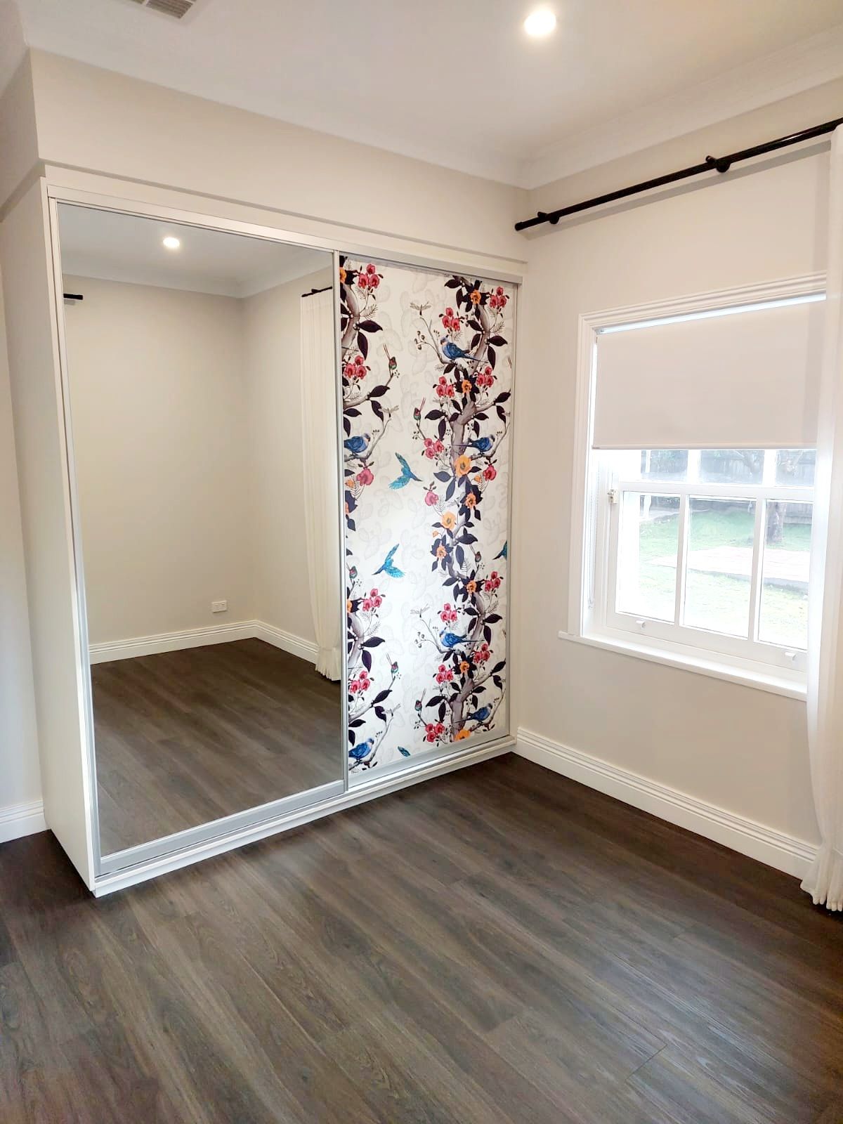 Bedroom With Dark Wood-look Floor, White Walls, and a Sliding Door Wardrobe With Mirror and Floral Design — Elimar Construction in Goulburn, NSW