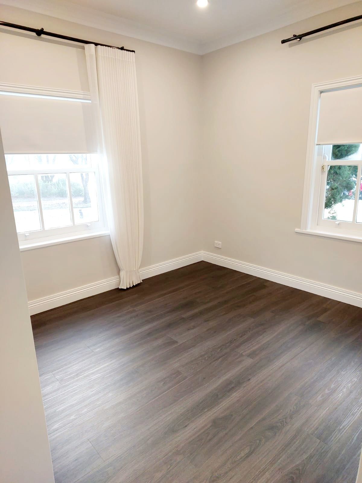 Empty Room With Dark Wood-look Floor, White Walls, Two Windows With Roller Blinds, and White Curtains — Elimar Construction in Goulburn, NSW
