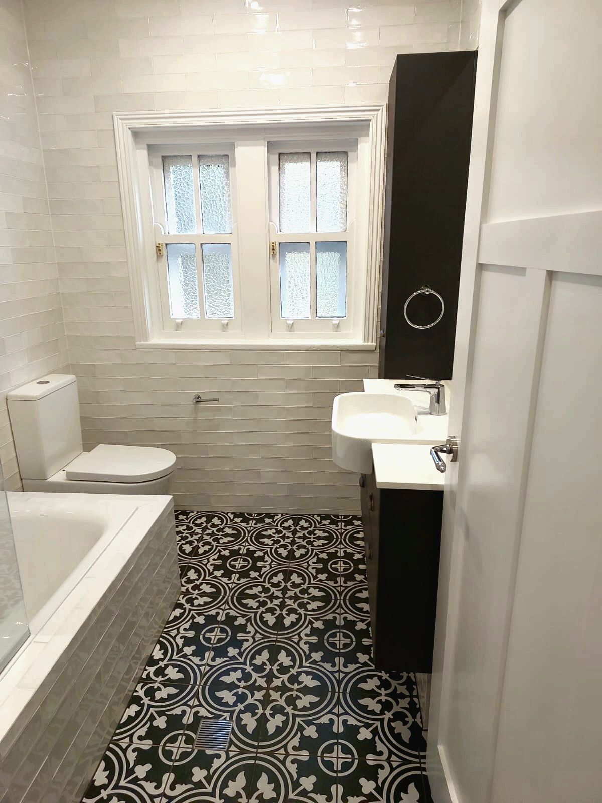Bathroom With Black and White Patterned Floor, White Walls, Toilet, Sink, and Tall Black Cabinet — Elimar Construction in Goulburn, NSW