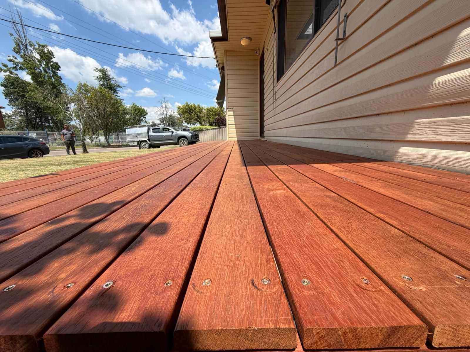 Low-angle view of a red wooden deck beside a house under a blue sky, with parked cars and trees in the distance — Elimar Construction in Goulburn, NSW