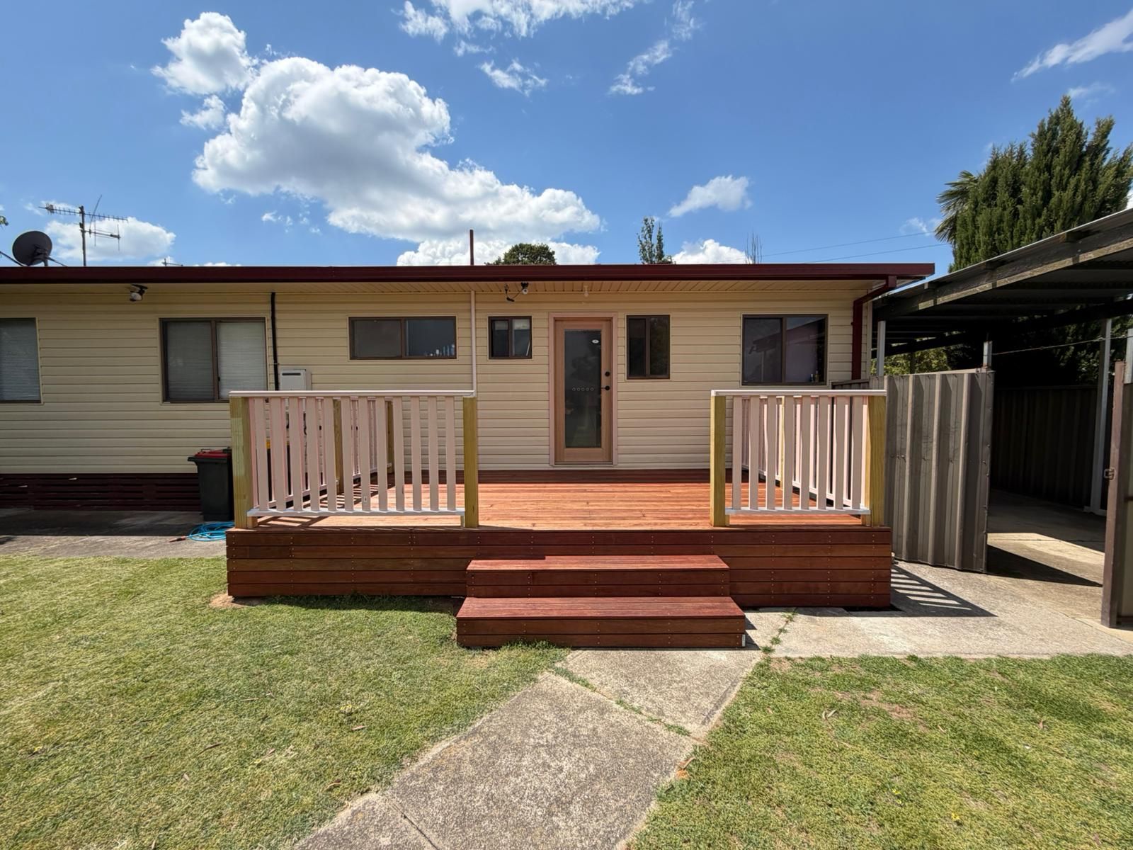 Single-story house with a small wooden deck, steps, and white railings in a sunny yard — Elimar Construction in Goulburn, NSW