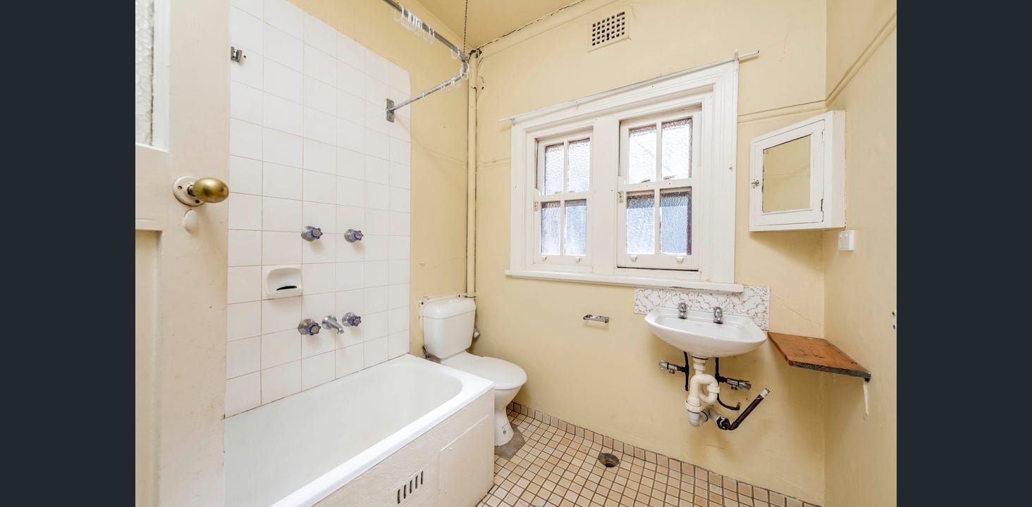 Small, Yellow-walled Bathroom With a White Bathtub, Toilet, and Sink. Windows and a Small Cabinet on the Wall — Elimar Construction in Goulburn, NSW