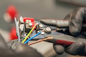 The electrician cleans the protective insulation from the wire using a wire stripper.