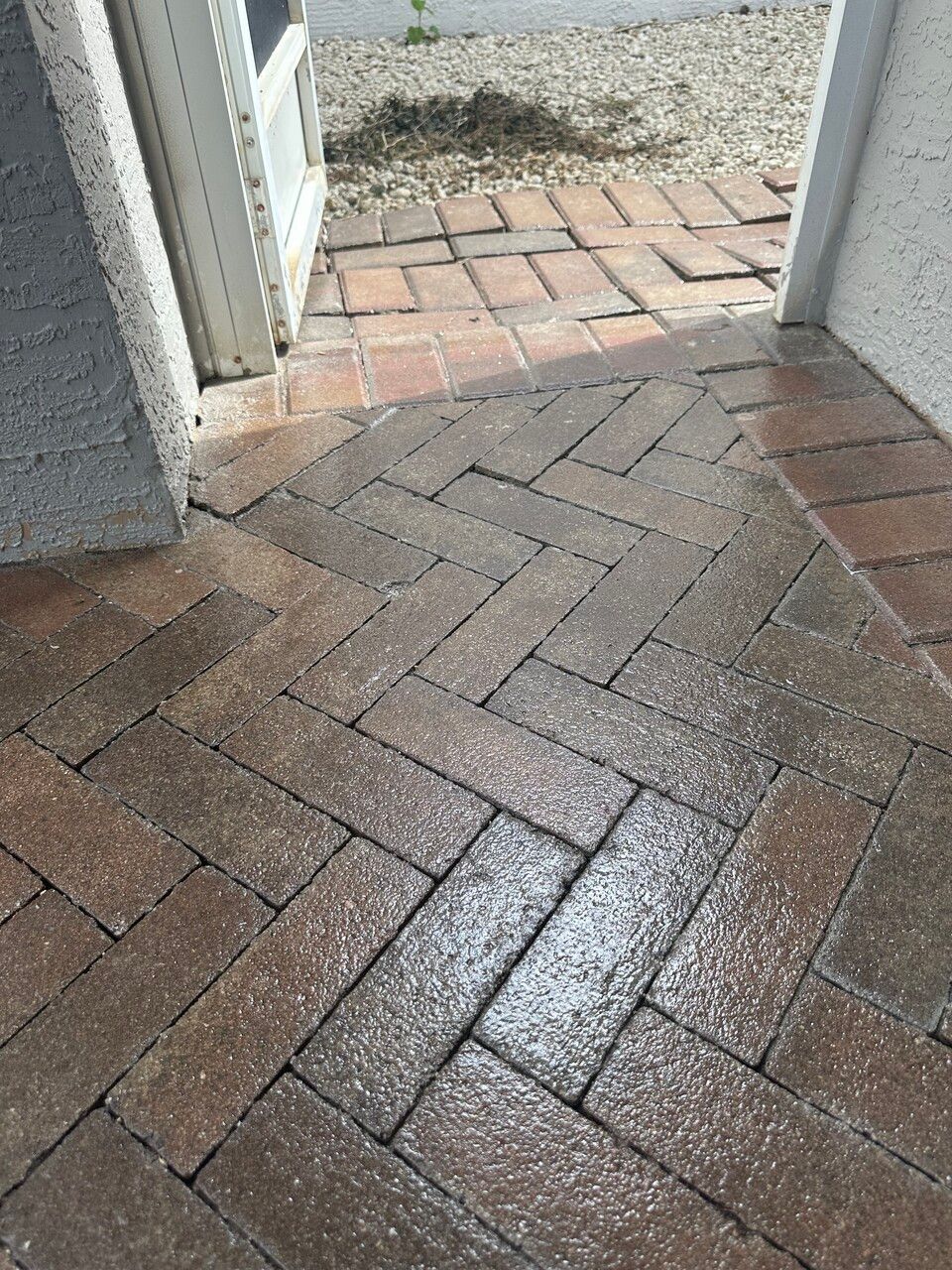a brick walkway with a herringbone pattern and a door in the background