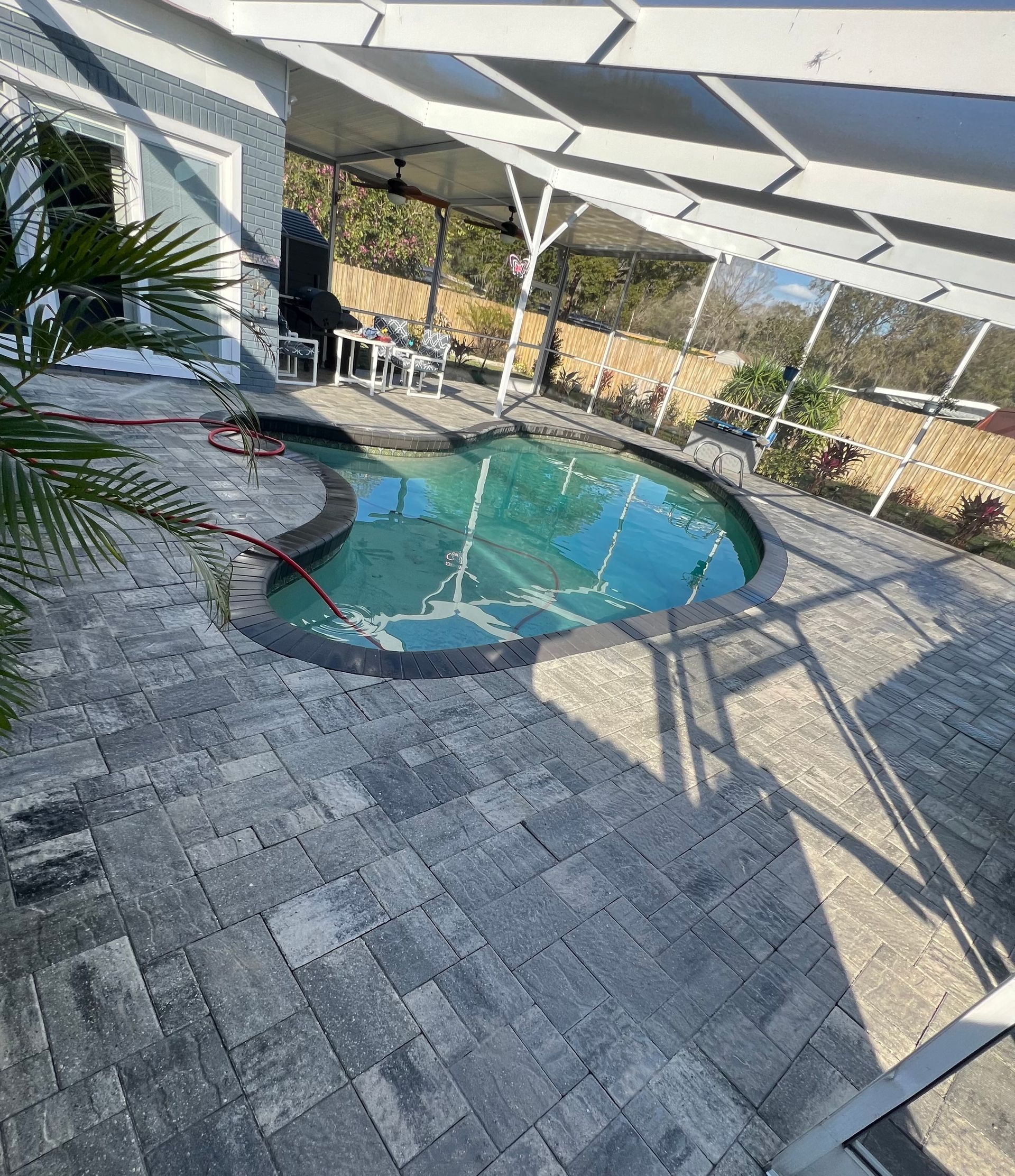 Pool with pavers, screened patio, and house. Blue water and gray brick ground.