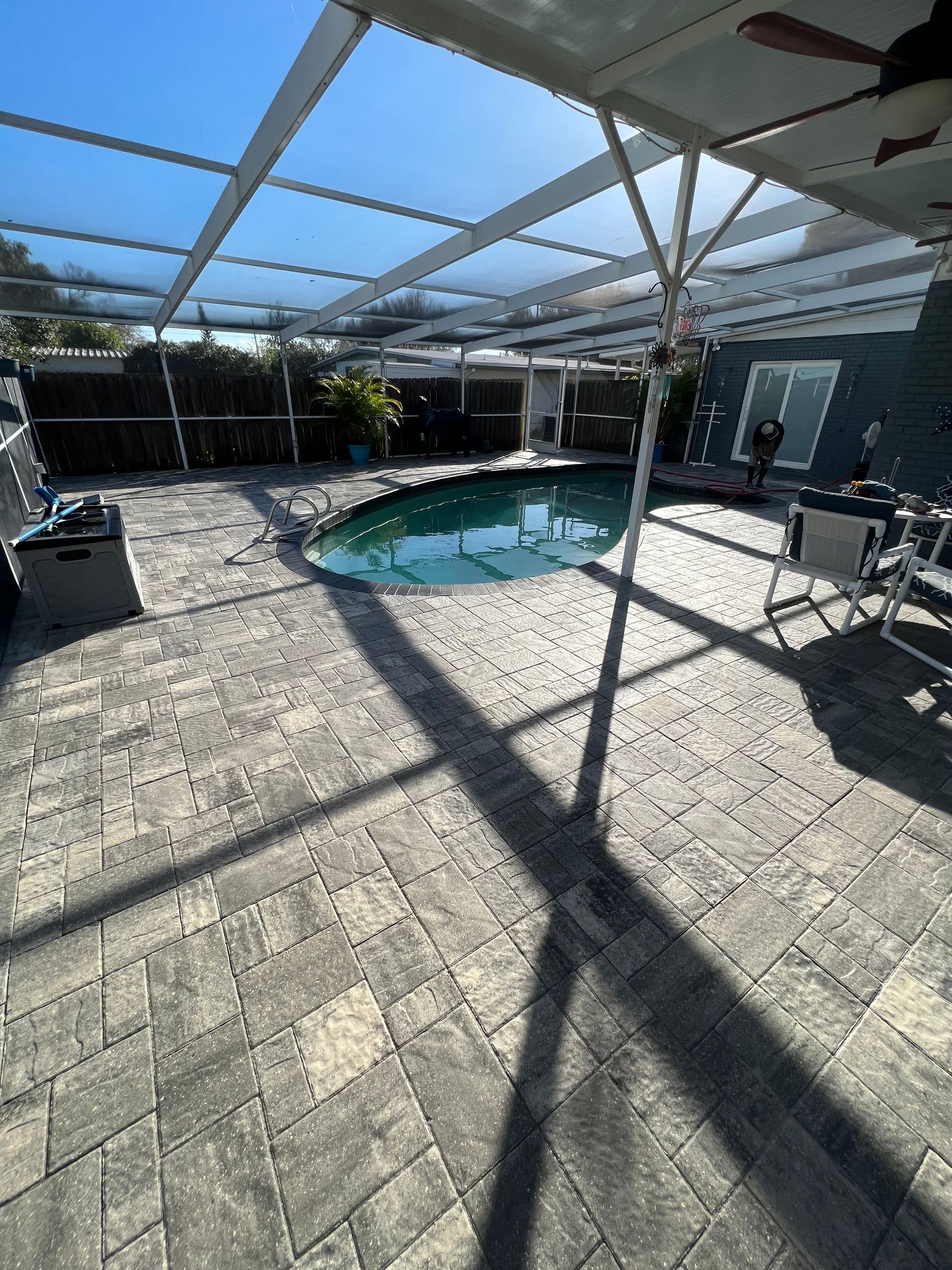 Patio with a screened pool, paved with grey bricks, under a bright blue sky.