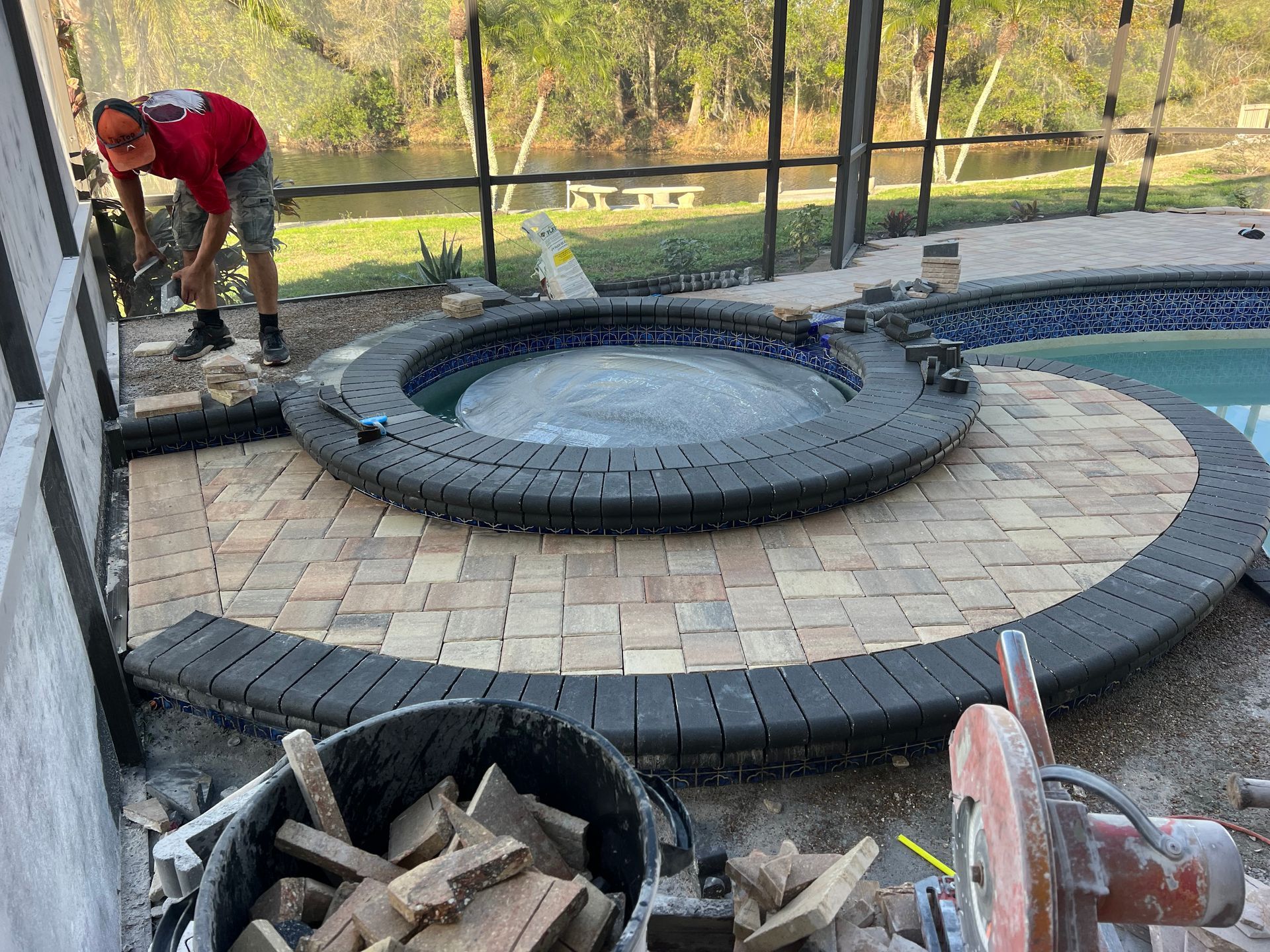 Man laying brick pavers around a hot tub next to a pool.