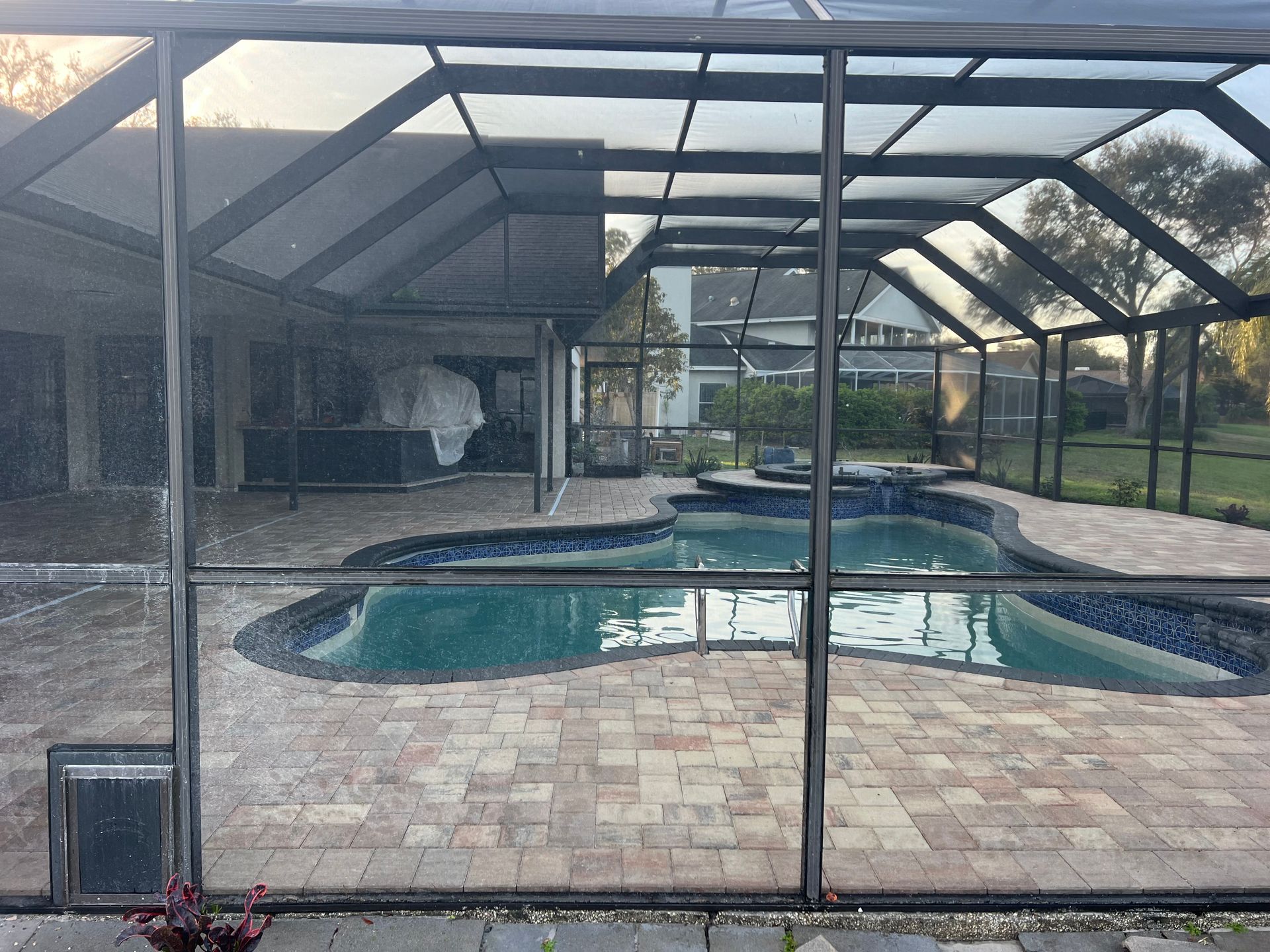Pool area enclosed by a black screened structure with a blue-tiled pool, brick pavers, and a small pet door.