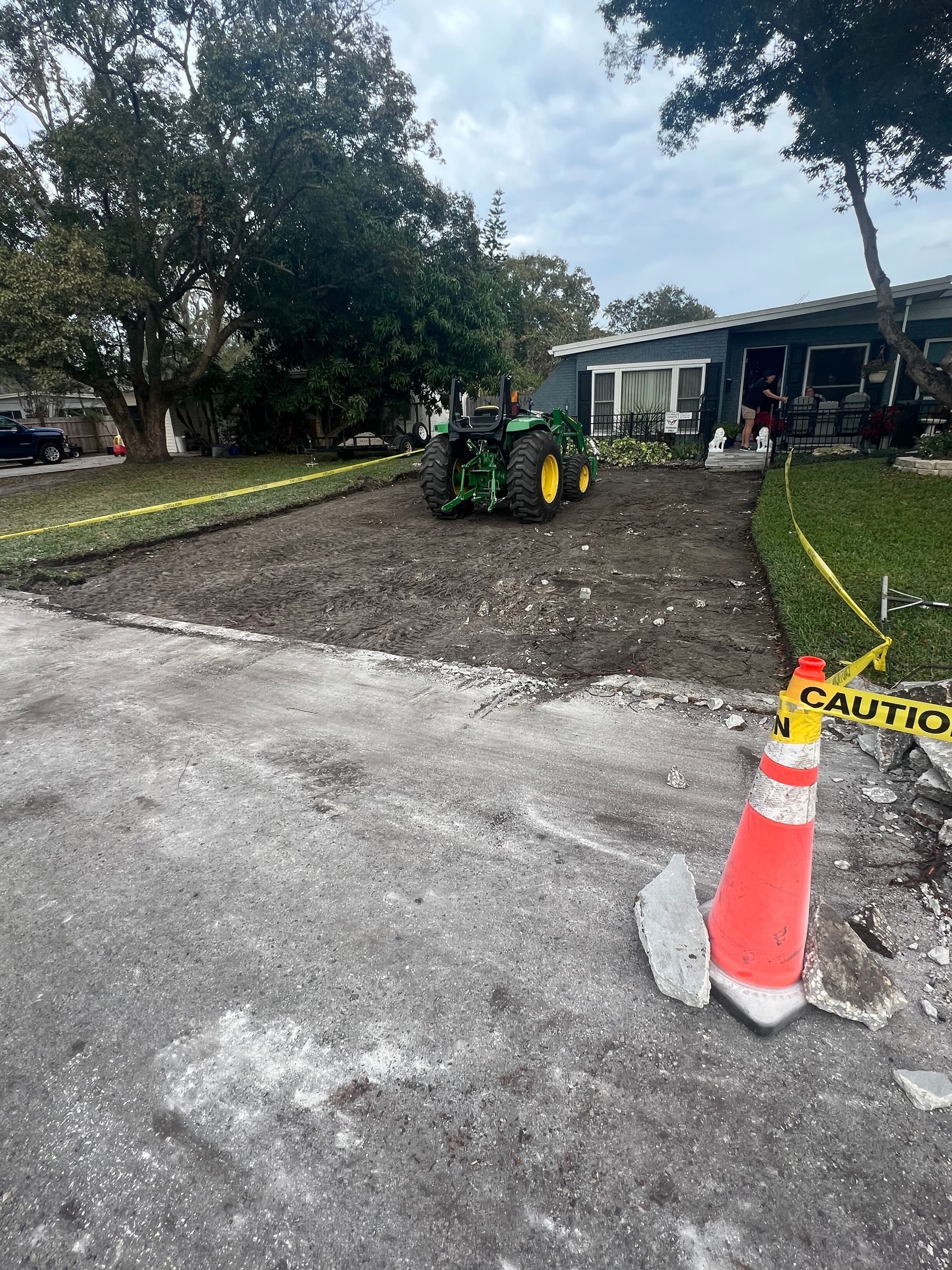 Driveway under construction with a tractor, caution tape, and orange cone.