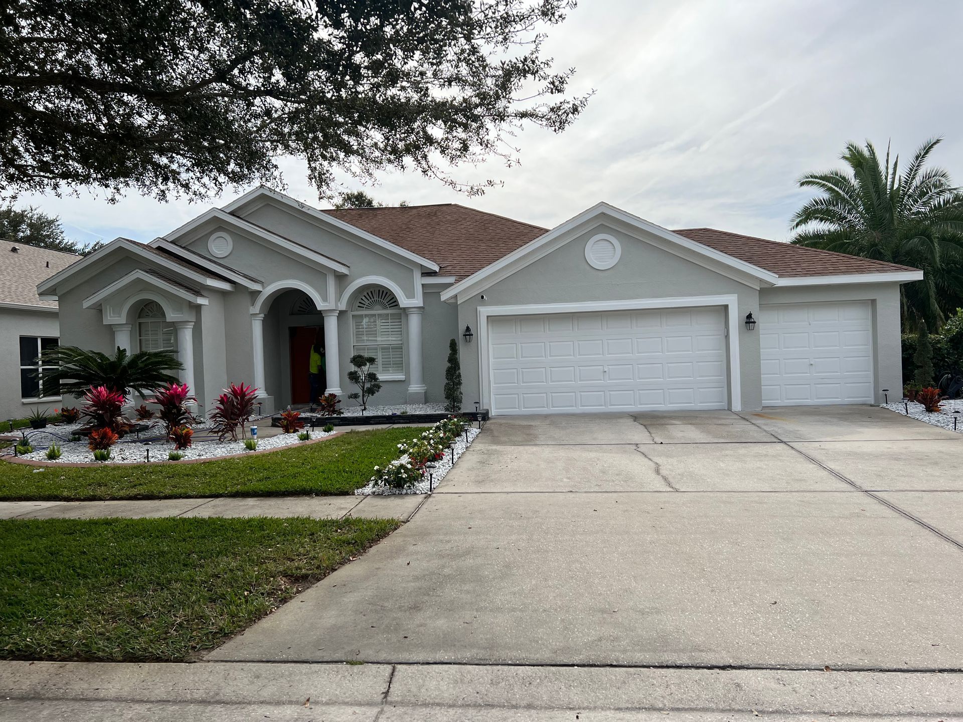 A light gray house with a red front door, white garage doors, and manicured landscaping.