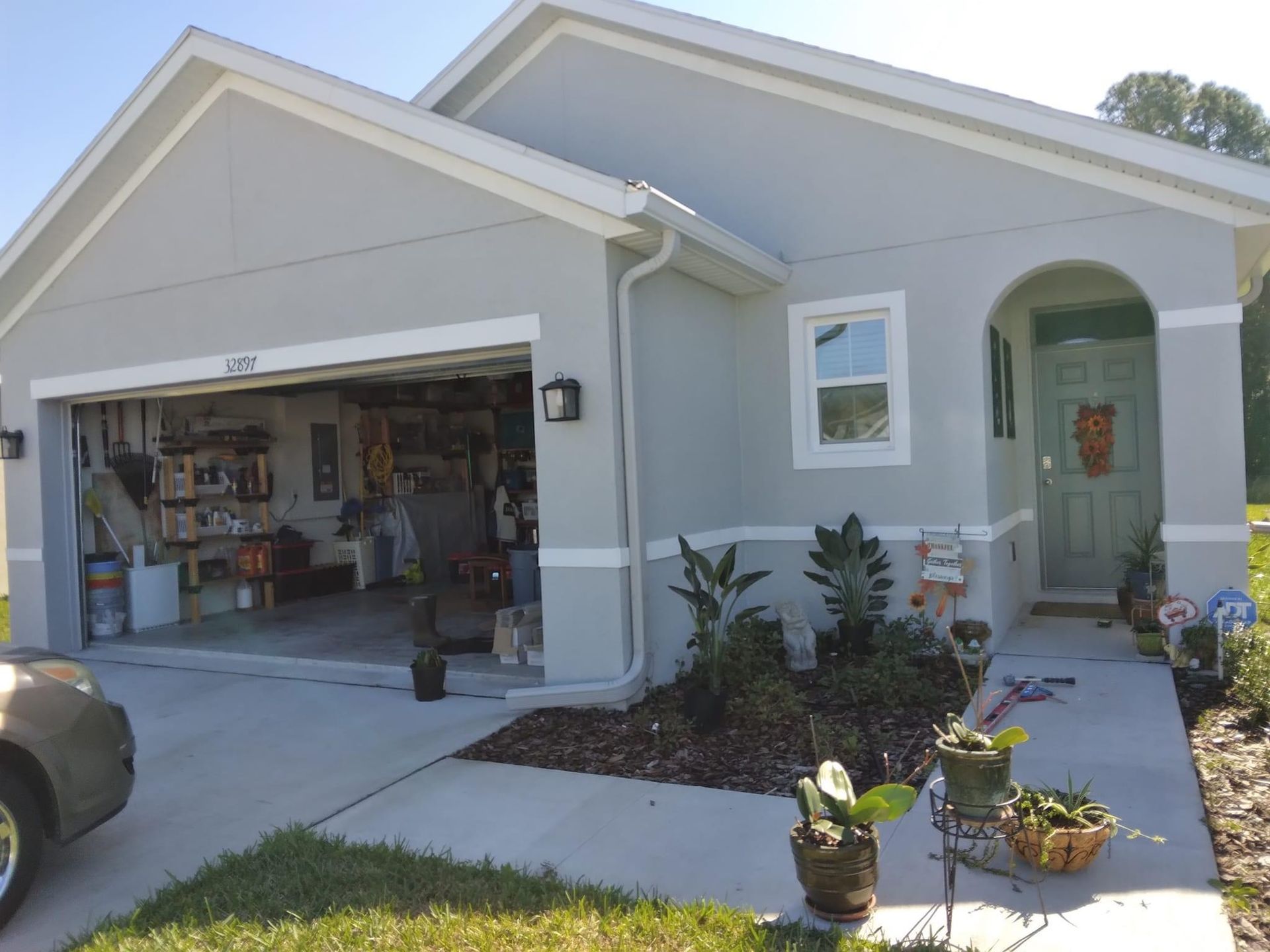 Light gray house with open garage; green front door. Landscaping and concrete driveway.