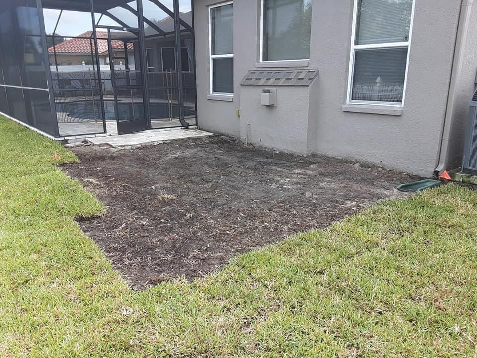 Backyard patio area with bare soil, next to a house and a screen-enclosed pool.