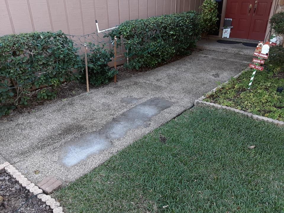 Driveway with gravel and a large concrete patch, bordered by grass and shrubs.
