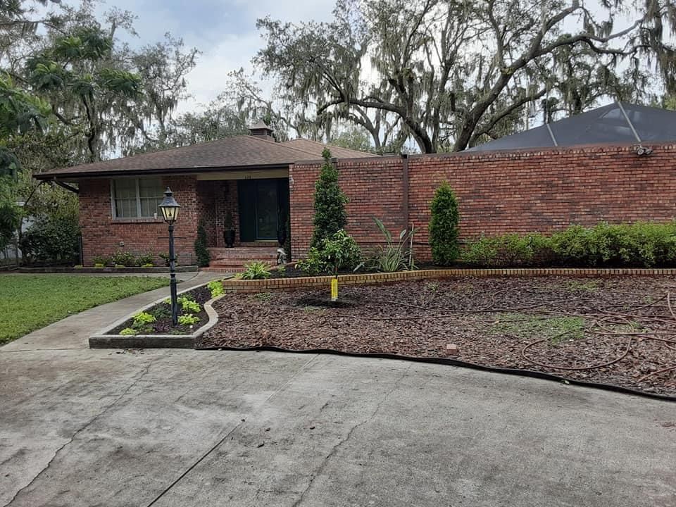 Brick house with a brick wall and a driveway. Landscaped front yard with dark mulch.