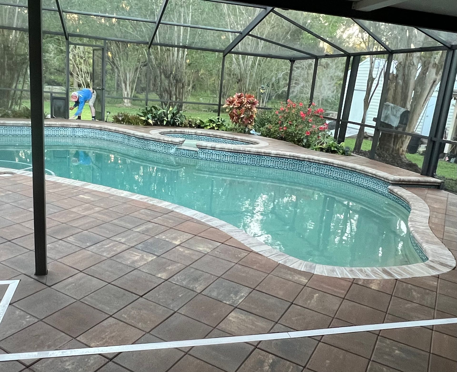 Pool surrounded by paver patio, screened enclosure, and landscaping.