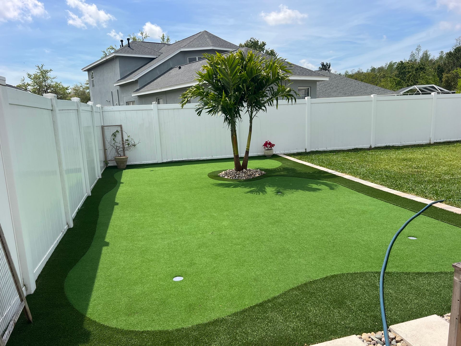 Green artificial turf backyard with a tree and white fence.