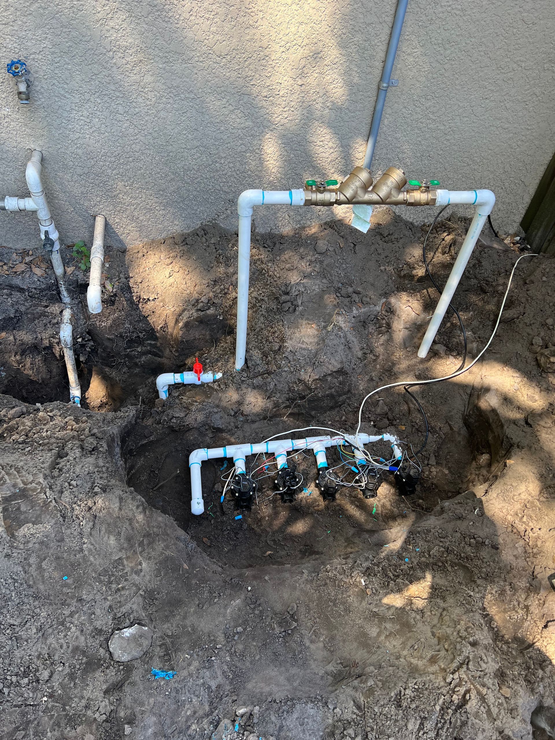 Irrigation system with PVC pipes, valves, and dirt. Outdoors.
