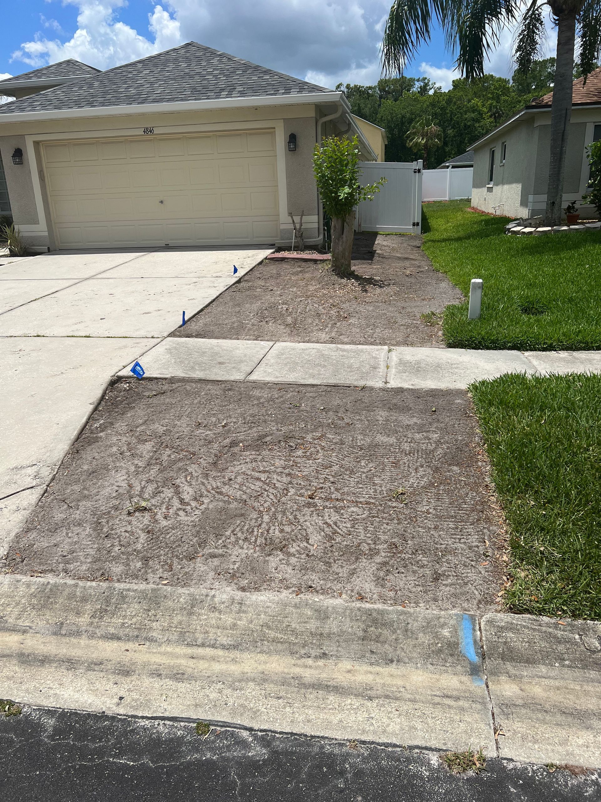 Front yard with driveway, flower beds, and house with beige garage door on a sunny day.
